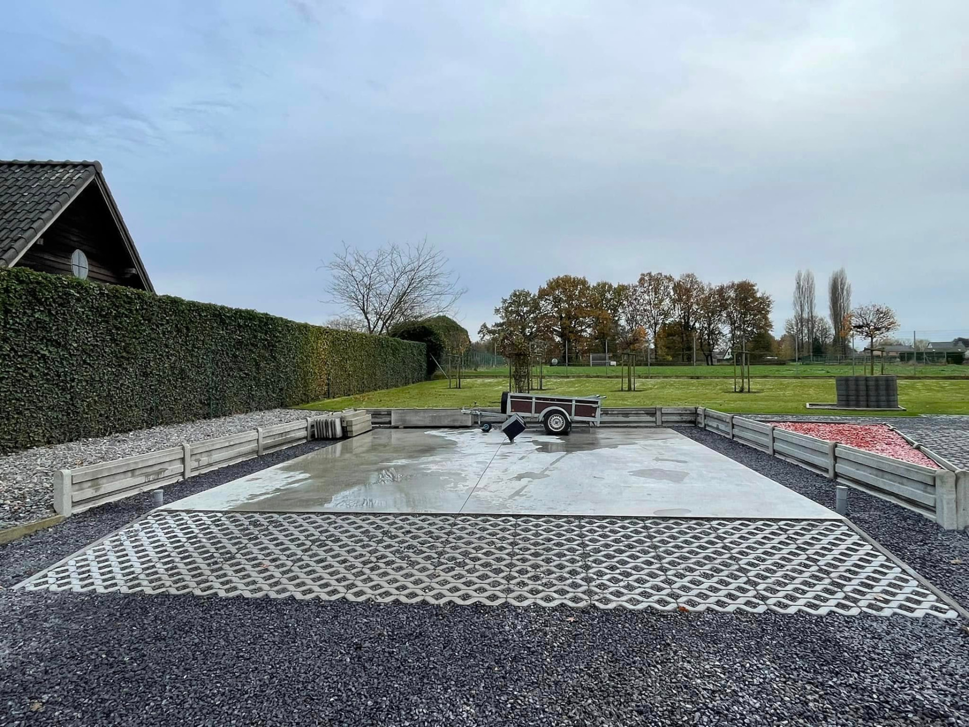 Betonnen verharding met grasdallen, omringd door grind en betonnen keerwanden